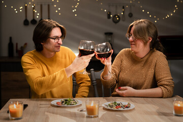 Real couple clinking and drinking with glasses of red wine at home. Celebrating Valentines Day