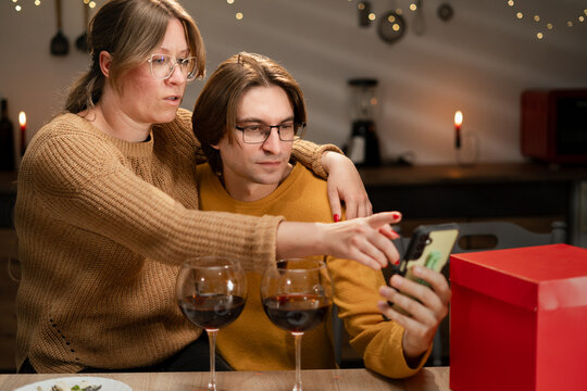 Smiling couple having romantic dinner at home, watching videos or reading social media news on smartphone. anniversary video.