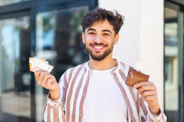 Handsome Arab man at outdoors holding wallet with money with happy expression