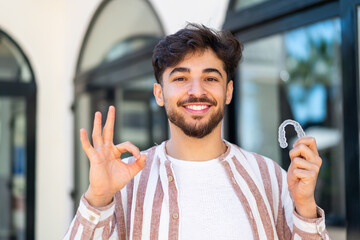 Handsome Arab man holding invisible braces at outdoors showing ok sign with fingers