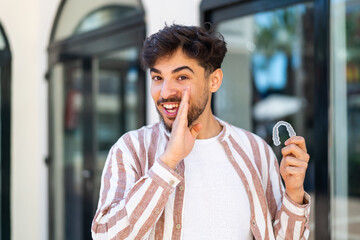 Handsome Arab man holding invisible braces at outdoors whispering something