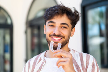 Handsome Arab man at outdoors holding invisible braces with happy expression