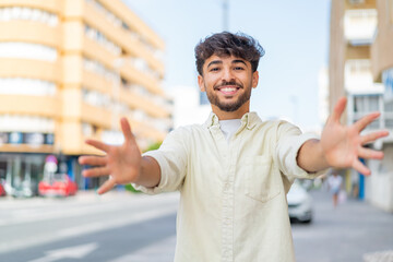 Young Arabian handsome man at outdoors presenting and inviting to come with hand