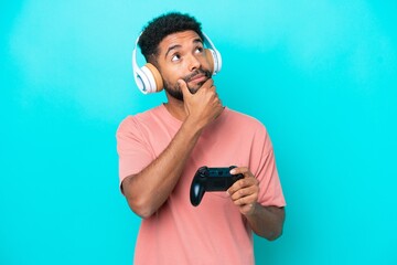 Young brazilian man playing with a video game controller isolated on blue background having doubts