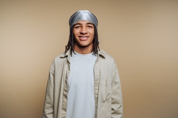 Young man with braided hair wearing a durag and casual clothing against a beige background.