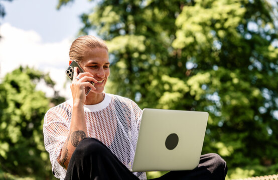 Modern woman working remotely in city park with laptop and smartphone