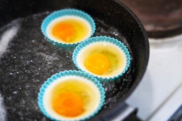 Three poached eggs cooking in blue silicone molds in boiling water on a stove