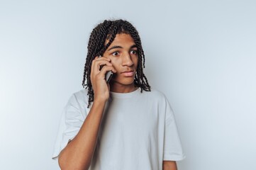 Young man with dreadlocks talking on a smartphone against a white background.