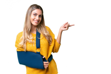 Young Uruguayan woman with broken arm and wearing a sling over isolated background pointing finger to the side