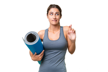 Pretty Young Uruguayan sport woman going to yoga classes while holding a mat over isolated background with fingers crossing and wishing the best