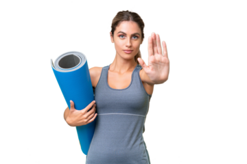Pretty Young Uruguayan sport woman going to yoga classes while holding a mat over isolated background making stop gesture