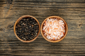 Two wooden bowls with pink salt and black peppercorns