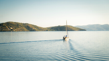A small sailing boat gliding through calm blue waters near the Greek islands during a warm summer evening. The peaceful scene captures the essence of Mediterranean travel, island hopping, and relaxed