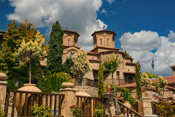 Exterior view of a historic Eastern Orthodox monastery built from stone with traditional Byzantine-style architecture, terracotta roof tiles, wooden stairways and large ceramic pots with plants