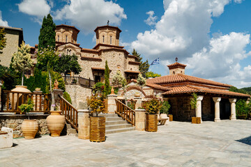 Exterior view of a historic Eastern Orthodox monastery built from stone with traditional Byzantine-style architecture, terracotta roof tiles, wooden stairways and large ceramic pots with plants