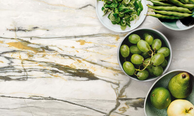 Fresh green vegetables and juicy fruits arranged on a marble surface for healthy cooking inspiration