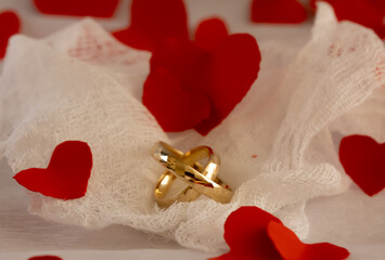 Gold Wedding Rings on Airy Gauze &ndash; Romantic Anniversary.  Artistic composition of gold wedding rings on light gauze fabric with red heart confetti, warm light, and shallow depth of field, expressing 