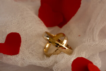 Romantic Wedding Rings on Gauze with Heart Confetti. Close-up of gold wedding rings on textured gauze background accented with red confetti hearts, combining softness, contrast, and romantic symbolism