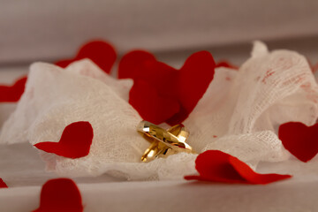 Wedding Rings on Soft Gauze and Red Hearts &ndash; Anniversary Concept. Delicate still life of gold wedding rings on airy gauze fabric with scattered red heart-shaped confetti, symbolizing love, care
