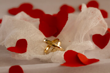 Gold Wedding Rings on Gauze with Red Heart Confetti &ndash; Wedding Anniversary. Romantic composition of gold wedding rings placed on soft gauze fabric decorated with red heart confetti