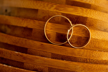 Gold Wedding Rings in Natural Light on Wood. Gold wedding rings photographed on wood using soft natural light, warm colors, and shallow depth of field, symbolizing lasting relationship and stability.