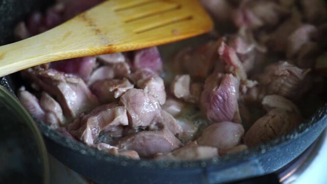 Close-up slow motion of chicken gizzards simmering in a pan on low heat