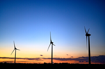 Obraz premium Beautiful colourful sunset silhouettes of wind turbines, windmill, copy space.