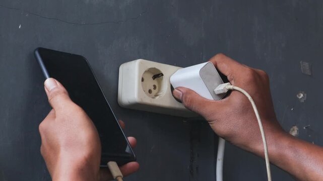 Asian male hand view plugging mobile phone charger cable into wall socket. Ready to connect, connect electricity.