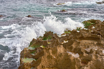Sunlit Shoreline: Waves Crashing on Rocky Coast