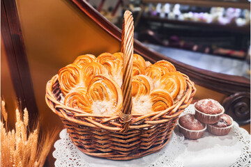 Sweet freshly baked braid buns with sugar powder in a wicker basket on table, closeup. Homemade organic French baking. Pastry background.