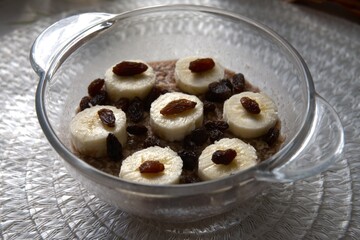 Healthy breakfast of chocolate oatmeal topped with banana slices and raisins in close-up view.