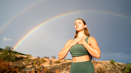 Woman meditating outdoors in nature in morning sunlight with double rainbow in background