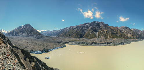 Looking over the moraine wall to the face of an alpine glacier breaking off icebergs and dropping...