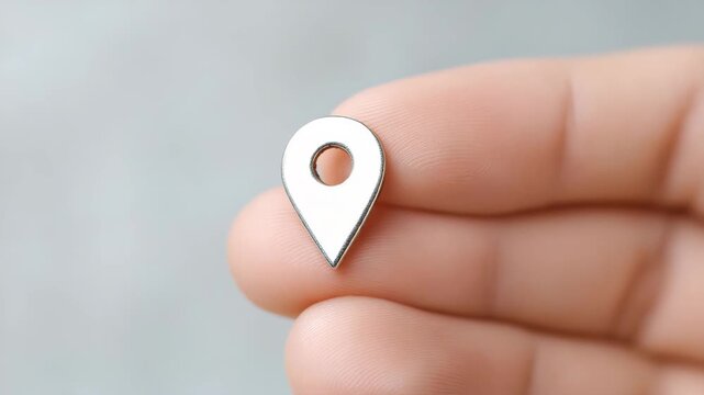 Metal location pin, navigation symbol, and map marker icon held between fingers, representing travel, direction, positioning, and technology with modern, minimalistic style, evoking curiosity