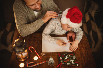 Happy father and son writing letter to Santa Claus together at home before Christmas, family bonding, holiday traditions, cozy festive atmosphere, childhood dreams, Xmas magic, wish list, top view
