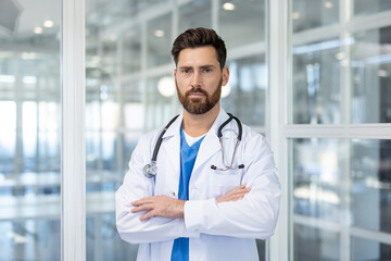 Confident male doctor finding himself in a modern clinic or hospital setting, presenting a professional and ready-to-help image with arms crossed, conveying trust and expertise in healthcare