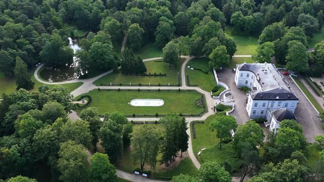Aerial view of a neoclassical mansion surrounded by lush greenery in Palanga, Lithuania. The estate features manicured gardens, a central fountain, and a statue in the foreground.