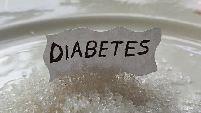 Diabetes word letters text handwritten calligraphy design on white paper label note isolated on top of pile of sugar. Closeup macro top view. Hyperglycemia Diabetes disease creative concept.