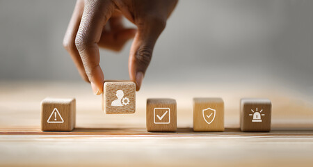 Wooden blocks with safety and compliance icons, African American hand arranging cube, workplace protection concept.