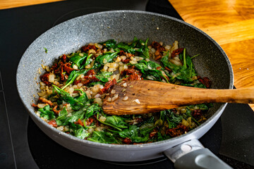 Frying spinach, onion and sun dried tomatoes in frying pan - cooking creamy Tuscan sauce