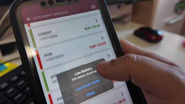 Mobile banking app displaying account details with low battery warning, prompting user to enable power-saving mode to conserve energy.