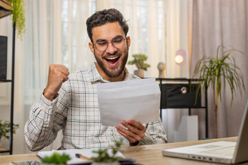 Happy excited Indian businessman manager open envelope letter, reading it. Career growth advance promotion bank loan approval successful admission to monetary award, long-awaited invitation great news