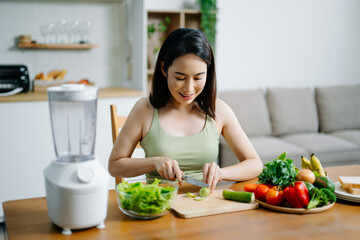 Smiling woman making healthy salad in modern kitchen with fresh greens, fruits, and blender. A clean eating and wellness lifestyle concept in a bright home