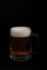 Dark beer in glass mug on black background – studio glassware