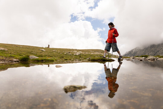 A woman in a red jacket is walking across a field of grass - Powered by Adobe