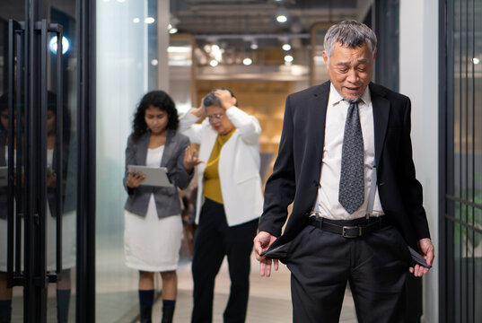 A man in a suit show empty pocket while walking through a modern office. Two employee react, one look at a tablet while the other show concern. The atmosphere is tense.
