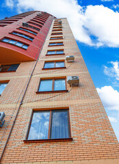 A tall modern brick apartment building with many windows and air conditioners against a blue sky...