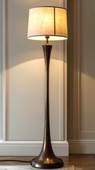 Tall, slender floor lamp with a beige shade, illuminated, standing against a neutral wall
