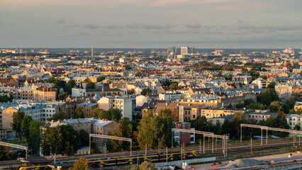 Panoramic cityscape featuring a railway station in the foreground, with train tracks, platforms, and multiple trains leading toward the urban skyline in the distance.