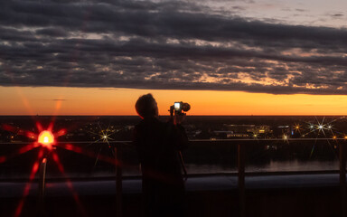 Sunset cityscape with a photographer capturing the beautiful view of the city at dusk. The warm evening light reflects on the skyline, creating a serene and atmospheric scene.